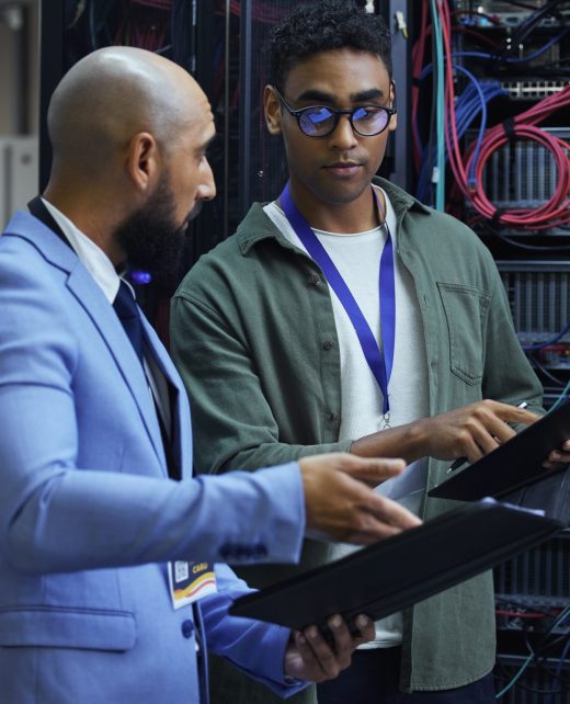 Cropped shot of two male IT support agents working together in a dark network server room.