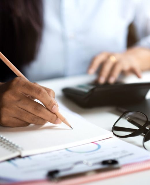 Close up of businessman or accountant hand holding pen working on calculator and laptop computer to calculate business data during make note at notepad, accountancy document at office.